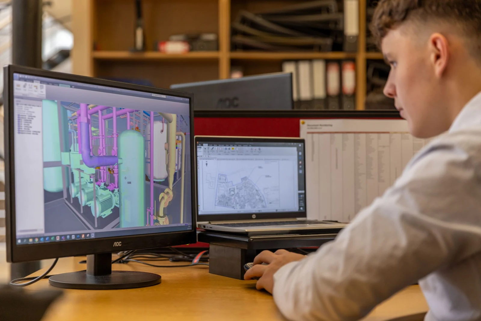 An engineer working at a desk with two monitors in a bright office