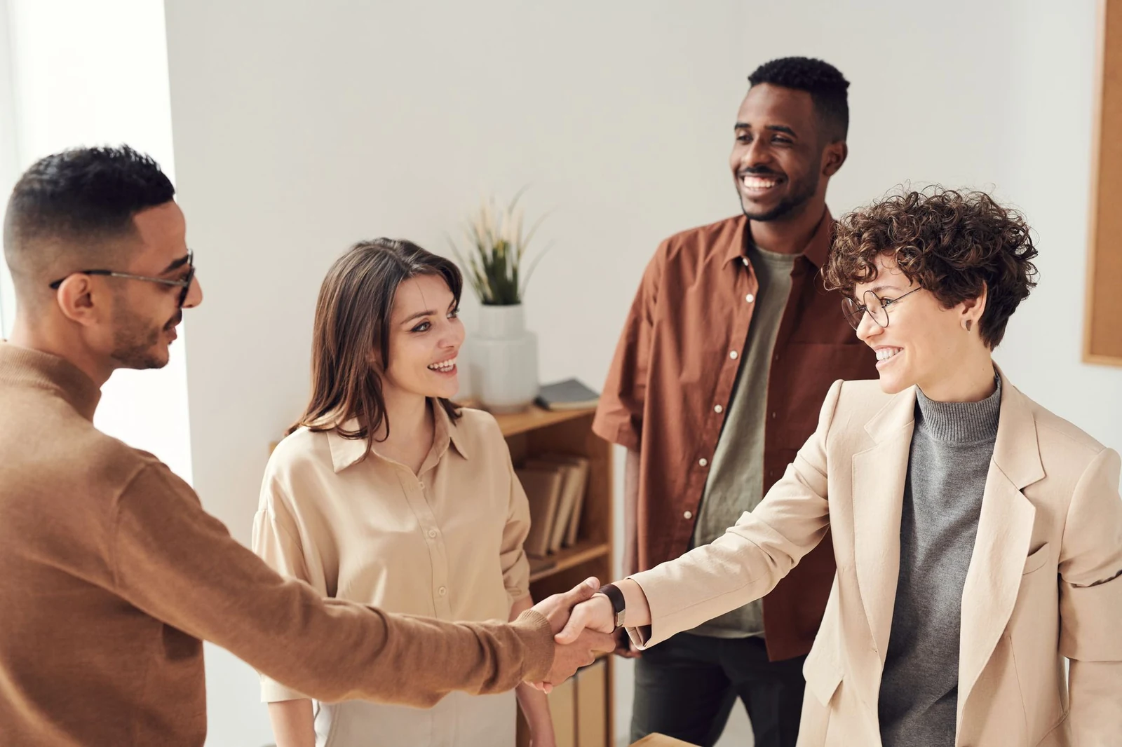 Two professionals shaking hands in a bright office as colleagues look on