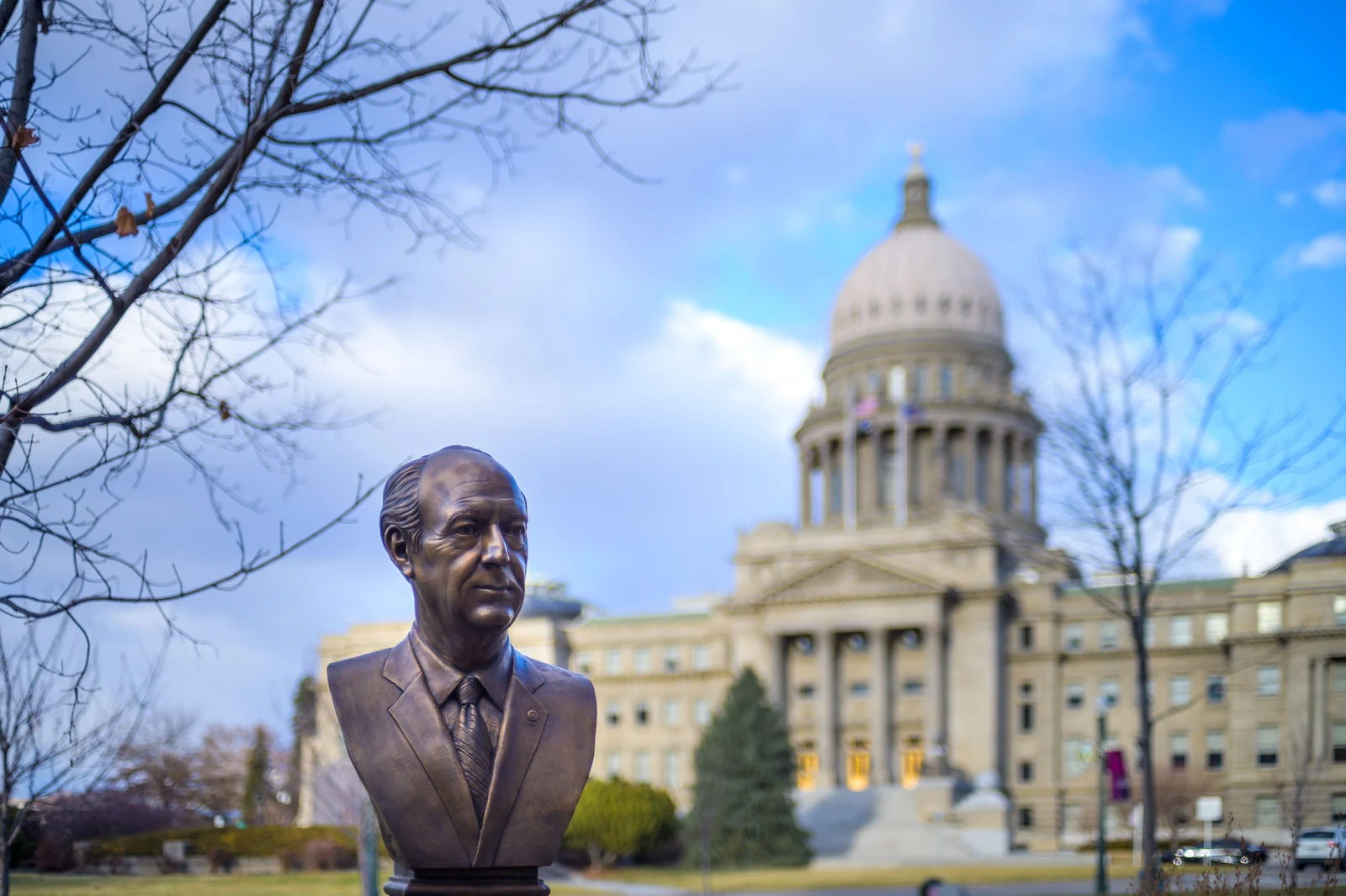 Bronze bust in the grounds in front of the domed Idaho State Capitol building in downtown Boise under a blue sky
