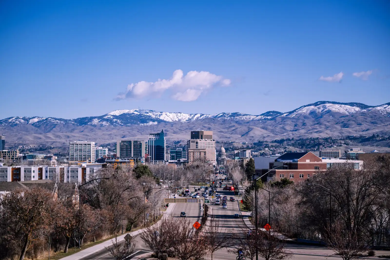 Capitol Boulevard leading into downtown Boise, Idaho, with the Idaho State Capitol dome, office towers and snow-covered foothills behind