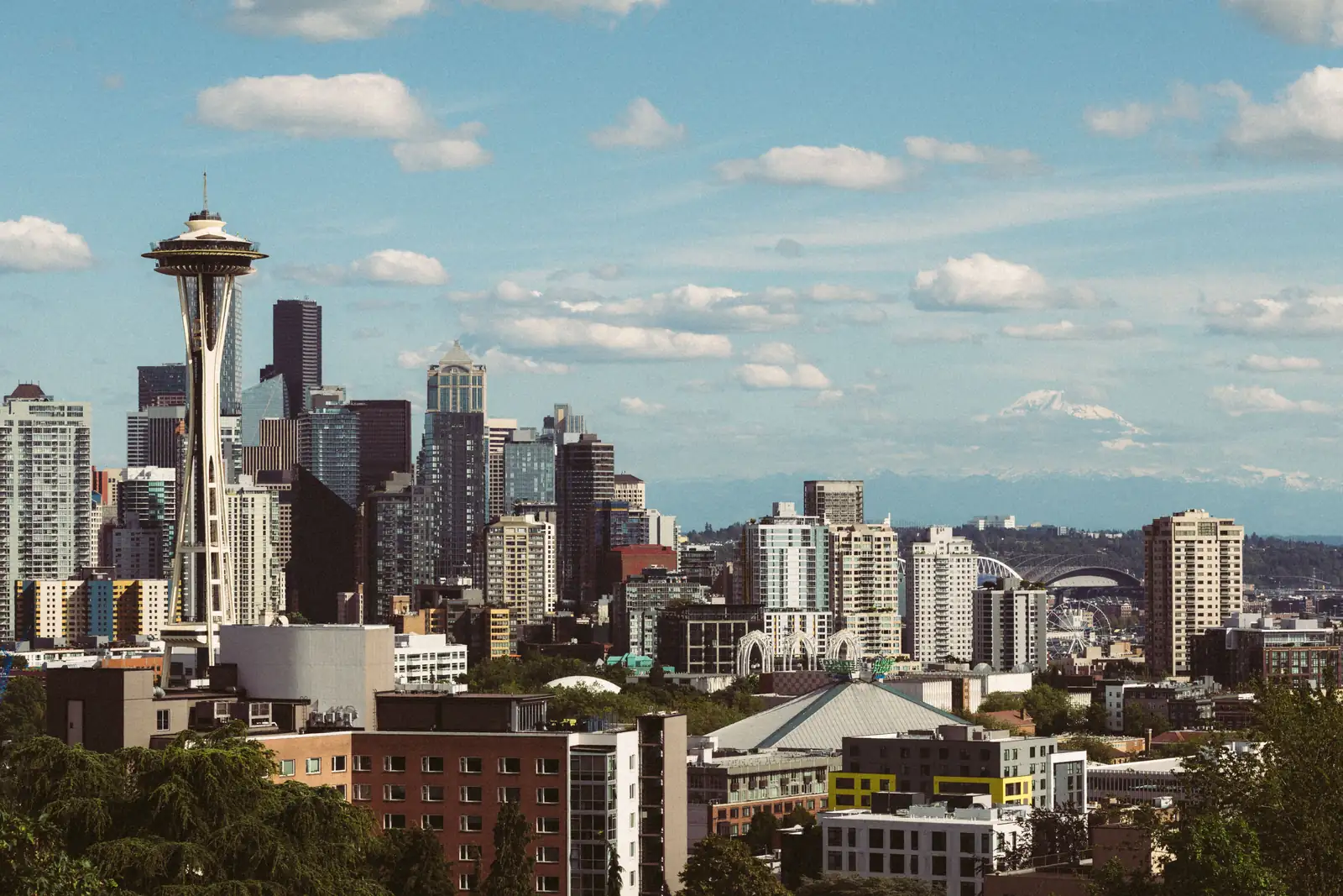 The Seattle skyline with the Space Needle on the left, downtown towers in the middle and snow-capped Mount Rainier on the horizon under a blue sky