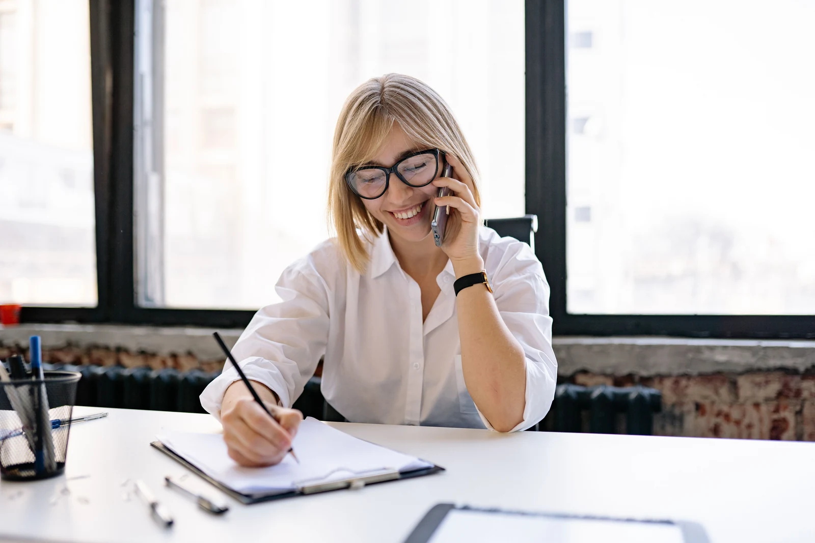 Smiling hiring manager on the phone taking notes at a bright office desk